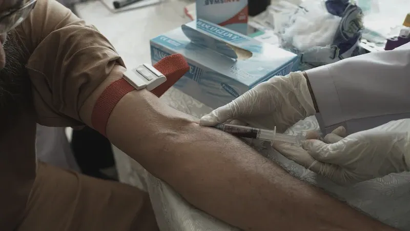 A gloved clinician drawing blood from a patient's arm