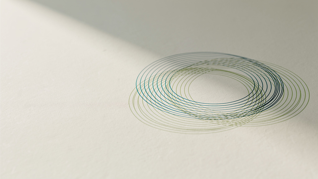 Two faint sets of concentric rings, one teal and one matcha, overlapping on a bone colored surface in soft daylight.