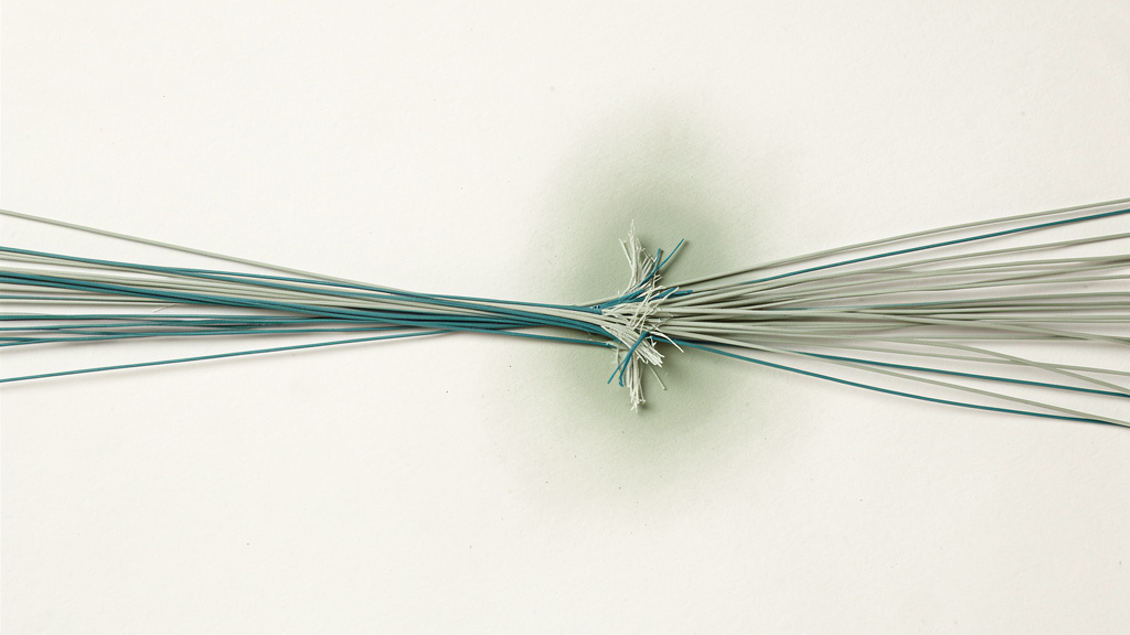 A bundle of fine sage and teal fibres drawn out lengthwise in a bone field, a few of them frayed where the pull is greatest, an abstract picture of lengthening strain on muscle.