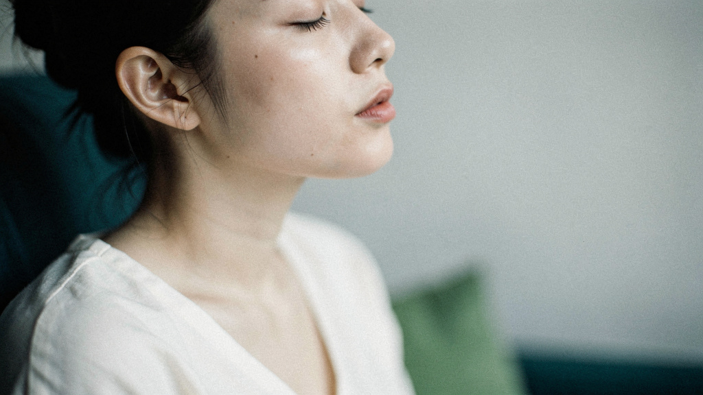 A close, calm portrait of a person mid-breath with soft shoulders in clean side light.