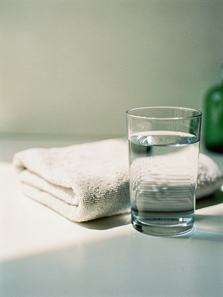 A clear glass of water beside a neatly folded towel in soft, clean light.