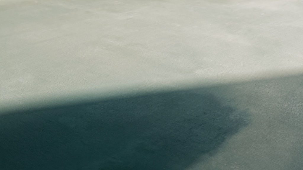 A calm, even surface lies untroubled while a single region of deeper tone rests just beneath it, unseen from above.