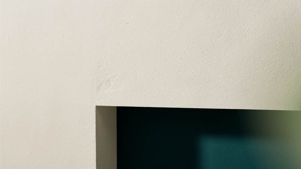 A still, matte bone-colored surface with a deep teal structure resolving into view beneath it and one faint matcha edge, an abstract image of an inherited trait set in place below a calm surface.